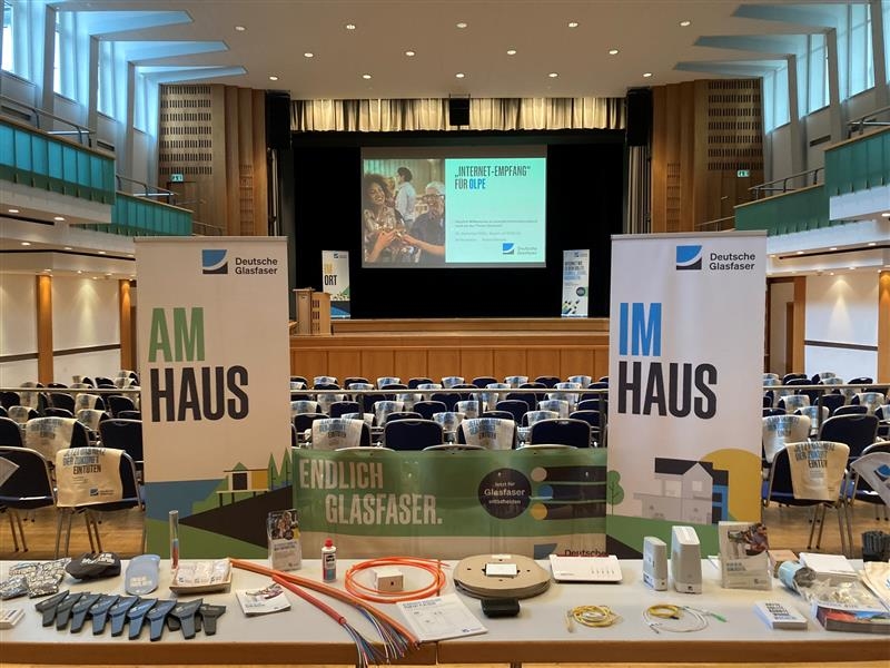 Blick vom Tisch der Vortragenden auf die bestuhlte Halle, Infobanner stehen rechts und links, beschriftet mit "Am Haus" und "Im Haus"